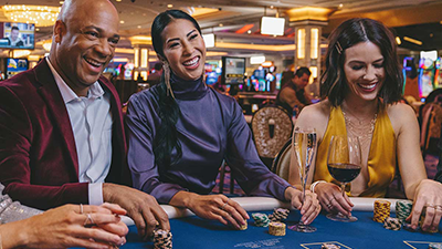 A group of smiling people gathered around a poker table.